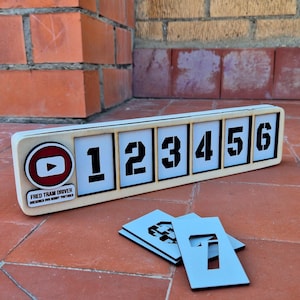 Peut inclure: Un présentoir de chiffres en bois avec les chiffres 1 à 6 en noir sur fond blanc. Le présentoir comprend un logo YouTube et le texte "FRED TRAM DRIVER DRESDNER DIY HOBBY YOUTUBER". Des pochoirs de chiffres sont devant.