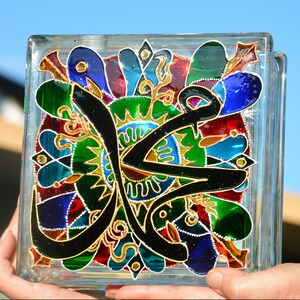 May include: A glass block with a colorful stained glass design featuring Arabic calligraphy and floral patterns in shades of red, green, blue, and gold.