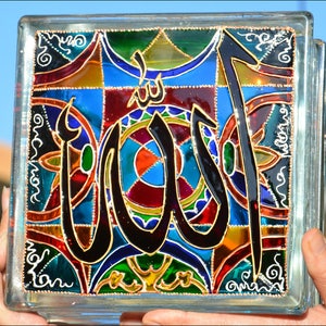 May include: A glass block with a stained glass design featuring the Arabic word "Allah" in black with gold accents. The background is a colorful mosaic of red, blue, green, yellow, and orange.