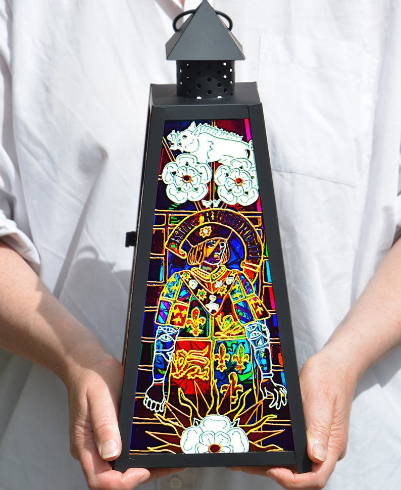 May include: A black metal lantern with a stained glass design. The glass features a colorful image of a person in armor, a white boar, and white roses. The text "RICARDUS III REX" is visible on the glass.