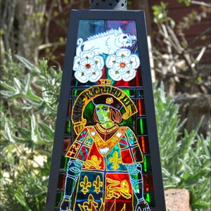 May include: A black metal lantern with stained glass depicting a man in a red and green coat with a white boar and white roses. The text "RICARDUS III" is visible in the stained glass.