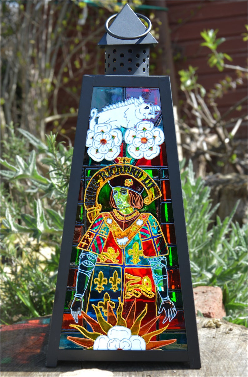 May include: A black metal lantern with stained glass depicting a man in a red and green coat with a white boar and white roses. The text "RICARDUS III" is visible in the stained glass.