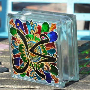 May include: A glass block with a colorful stained glass design featuring Arabic calligraphy and intricate patterns in shades of red, blue, green, gold, and black.