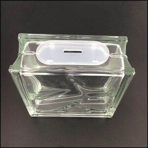 May include: A clear glass block with a white plastic slot on top. The slot has a small opening in the center.