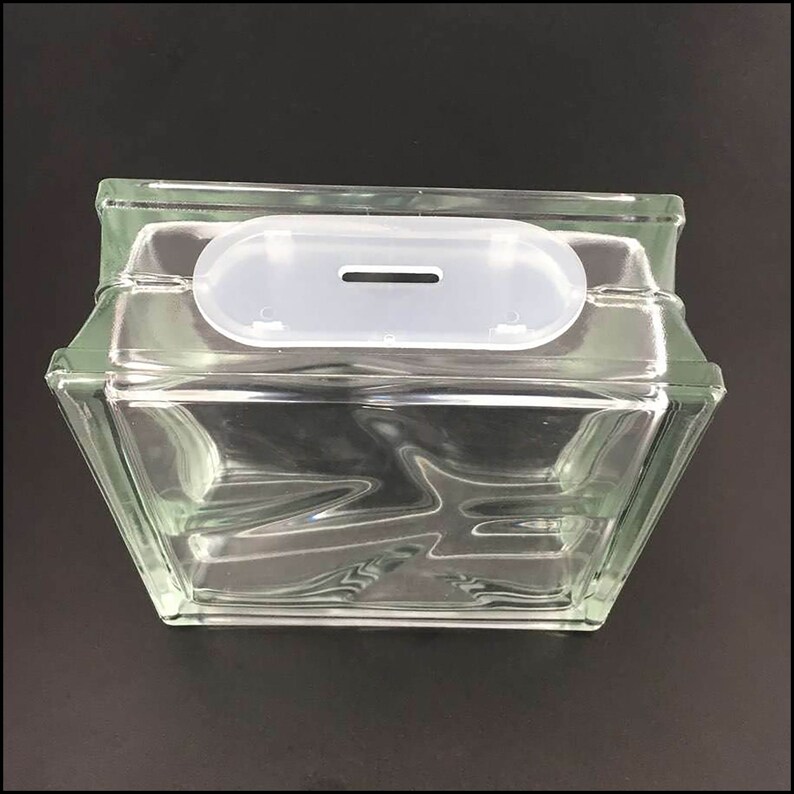 May include: A clear glass block with a white plastic slot on top. The slot has a small opening in the center.