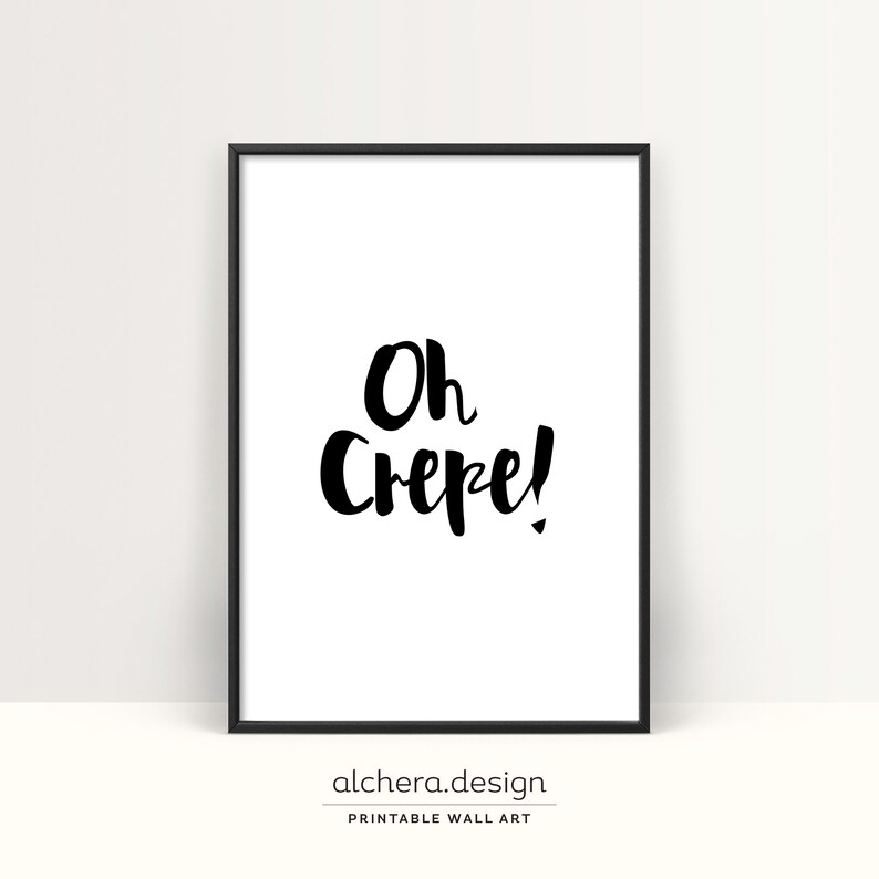May include: A rectangular wall art print in a thin black frame featuring a white background with the black hand-lettered text Oh Crepe! centered in the middle. The design uses a bold brush-style font to display the phrase clearly on the paper.
