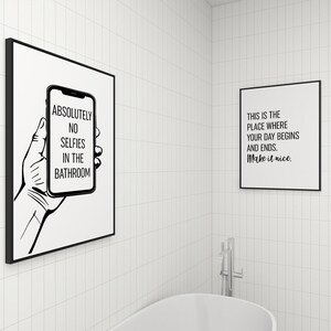 Two framed black-and-white art prints displayed on white tiled bathroom walls above a bathtub.