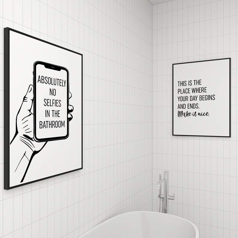 Two framed black-and-white art prints displayed on white tiled bathroom walls above a bathtub.