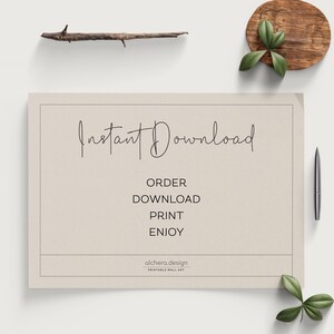 A light beige paper with "Instant Download" in script and "ORDER DOWNLOAD PRINT ENJOY" in block letters, next to a pen and green leaves on a white surface.