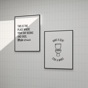 Two black-framed typographic and illustrated wall art prints hanging on white tiled walls.