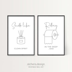 Two framed black and white line art prints: one of a diffuser with "Smells like clean spirit" and one of toilet paper with "Rolling in the deep...paper."