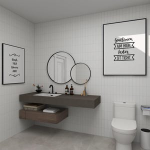 A modern bathroom interior featuring a white toilet, floating wooden sink vanity, and framed wall art.