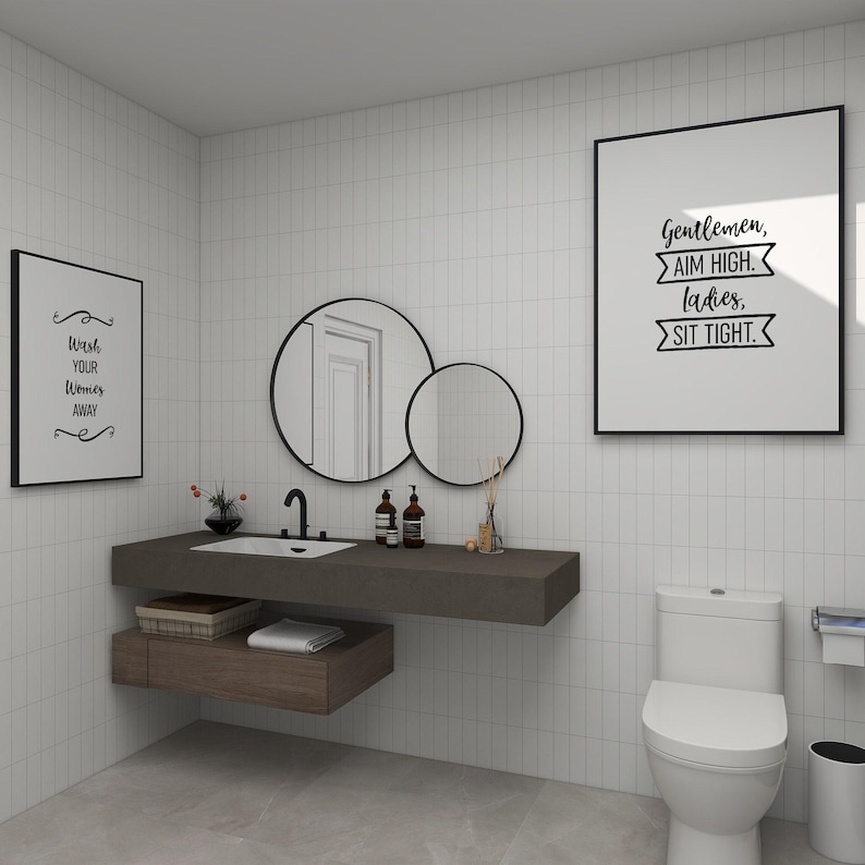 A modern bathroom interior featuring a white toilet, floating wooden sink vanity, and framed wall art.