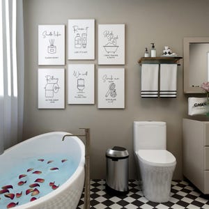 A bathroom with a white clawfoot tub, a toilet, and six framed black and white line art prints on the wall.