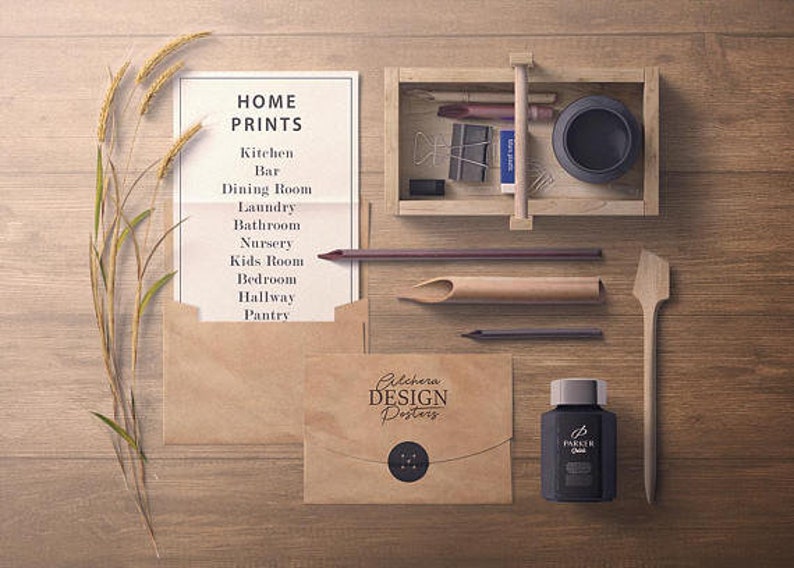 Puede incluir: Una vista a&eacute;rea de art&iacute;culos de papeler&iacute;a y decoraci&oacute;n del hogar sobre una superficie de madera. Incluye una lista titulada "HOME PRINTS", sobres, una caja de madera con art&iacute;culos de papeler&iacute;a, un frasco de tinta y una esp&aacute;tula de madera. El texto "Pilchera DESIGN Posters" es visible.