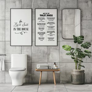 Two framed white posters, one with toilet jokes and one with "The Best Seat in the House," hang above a toilet in a gray tiled bathroom with a plant and mirror.