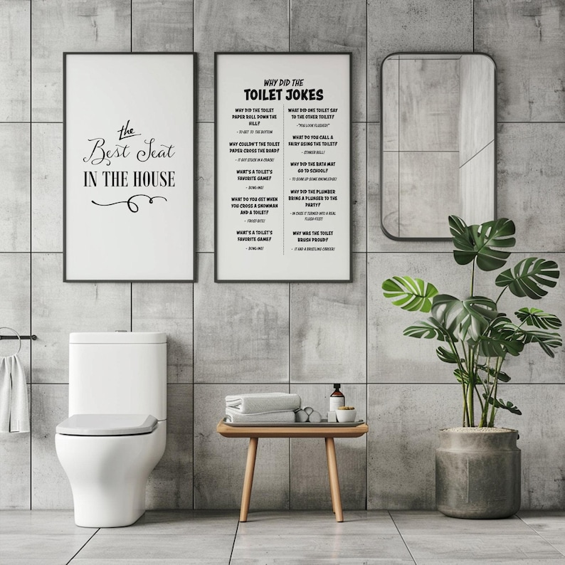 Two framed white posters, one with toilet jokes and one with "The Best Seat in the House," hang above a toilet in a gray tiled bathroom with a plant and mirror.
