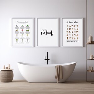 Three framed white prints hang above a white freestanding bathtub: one with essential oils, one saying "get naked," and one with ASL for "All Hands Welcome."