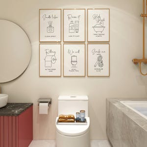 A bathroom with a toilet, a sink, and six framed black and white line art prints on a light-colored wall.
