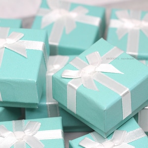 May include: A group of small, light blue gift boxes with white satin ribbon bows. The boxes are stacked and arranged in a random pattern. The boxes are ideal for packaging small gifts or jewellery.