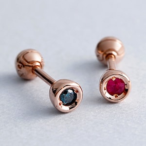 May include: A pair of gold stud earrings with a small blue gemstone on one and a small red gemstone on the other.