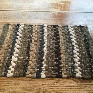 May include: A woven rug with a striped pattern in shades of brown, beige, and white. The rug is made of a thick, textured fabric and has a fringed edge.