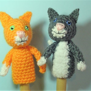 Peut inclure: Deux marionnettes à doigts en crochet, l'une orange et l'autre grise avec des accents blancs. La marionnette orange a des yeux verts et un nez rose. La marionnette grise a des yeux bleus et un nez rose.