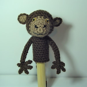May include: A handcrafted crochet monkey puppet. The monkey features a brown body, head, and arms, with a tan face and golden eyes. It is attached to a wooden dowel. Ideal for children's play or as a decorative piece. The puppet's height is approximately 25 cm.