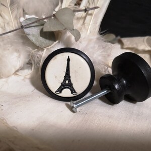 Puede incluir: Pomo de armario de cerámica blanco y negro con una silueta de la Torre Eiffel. El pomo está unido a un tornillo de metal negro.