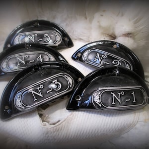 May include: Five black and silver drawer pulls with numbers 1 through 5. Each pull is shaped like a half-circle and has a raised, silver number on a black background.