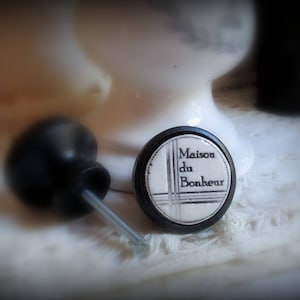 以下が含まれることがあります： 黒の縁取りと黒文字で「Maison du Bonheur」と書かれた白いセラミック製のノブ