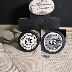 Puede incluir: Dos tapones de botella redondos negros y blancos con el texto "Jack Daniel's Old No. 7 Brand Tennessee Whiskey" en ellos.