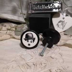 May include: Two black cabinet knobs with a white porcelain face. One knob features a black and white image of Charlie Chaplin.