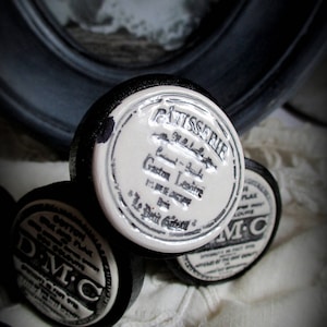 May include: Four vintage black and white ceramic jar lids with labels. The top lid has the text "Patisserie Gaston Lenotre Le Petit Gateau" in black lettering on a white background.