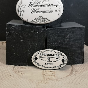 May include: Two white ceramic oval tags with black lettering. The top tag reads "Fabrication Française". The bottom tag reads "Apothecaire 1837".