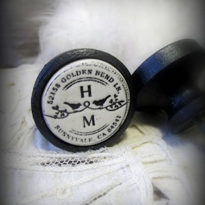 May include: Black and white ceramic knob with the text "32158 Golden Bend Ln. Sunnyvale, CA 94581" and the letters "H & M" with two birds on a branch.