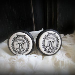 May include: Two black and white ceramic drawer knobs with a floral design and the text "Howard & Sons" in a circle.