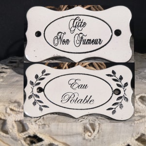 Peut inclure: Deux panneaux en céramique blanche avec des lettres noires. Le panneau du haut indique "Gite Non Fumeur" et le panneau du bas indique "Eau Potable".