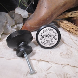 May include: Two black ceramic drawer knobs. One knob has a white ceramic insert with the text "LA SAMARITAINE LA MEILLEURE DE TOUTES LES LESSIVEUSES".