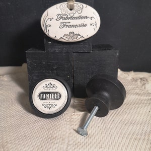 Peut inclure: Deux boutons en céramique noire avec des étiquettes ovales blanches. Une étiquette indique "FAMILLE" et l'autre "Fabrication Française".
