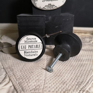 May include: White ceramic knob with black trim and the text "Source Minerale EAU POTABLE Bienfaits Naturels". The knob is attached to a black metal screw.