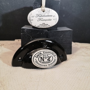 Peut inclure: Un bouchon de bouteille en céramique noire avec un logo blanc Jack Daniel's Old No. 7 Tennessee Whiskey. Une étiquette en céramique blanche avec le texte "Fabrication Française" est également représentée.
