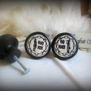 Puede incluir: Dos pomos de cerámica en blanco y negro con las palabras "Only Men" y "Only Women" en ellos. Los pomos están unidos a bases de metal negro.