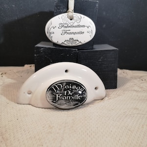 Könnte beinhalten: Weißer Keramik-Türknopf mit einem schwarzen ovalen Etikett mit der Aufschrift "Maison De Famille" und einem weißen ovalen Etikett mit der Aufschrift "Fabrication Française".