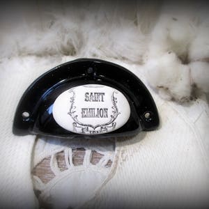 Puede incluir: Tirador de cajón de cerámica negra con una inserción ovalada de porcelana blanca que dice "Saint Emilion".