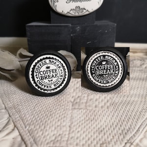 Peut inclure: Deux boutons en céramique noir et blanc avec les mots "Coffee Break" et un graphique de tasse à café. Les boutons sont ronds et ont un bord surélevé.