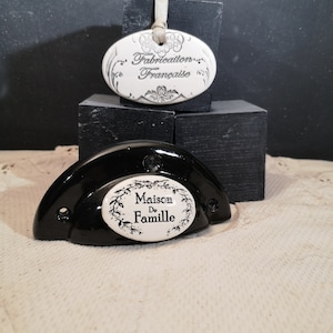May include: Two white ceramic oval-shaped tags with black lettering. The top tag reads "Fabrication Française" and the bottom tag reads "Maison de Famille".