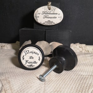 Peut inclure: Deux boutons de cabinet en céramique noire avec des inserts en porcelaine blanche. Les inserts présentent du texte français qui se lit "Maison De Famille" et "Fabrication Française".