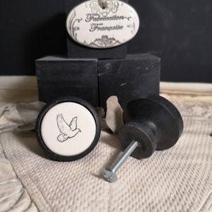 May include: Two black ceramic cabinet knobs with a white ceramic insert. One knob features a dove design and the text "Fabrication Française".