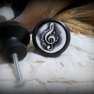 May include: Two black cabinet knobs with a silver screw. One knob has a white background with a black treble clef and musical notes.